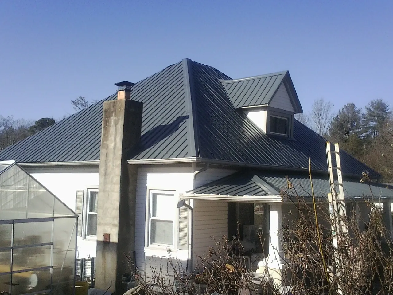 Dark blue standing seam metal roof on a white farmhouse with dormer — Slate & Tile Roof Repair by Roofing Brothers in North Lewisburg