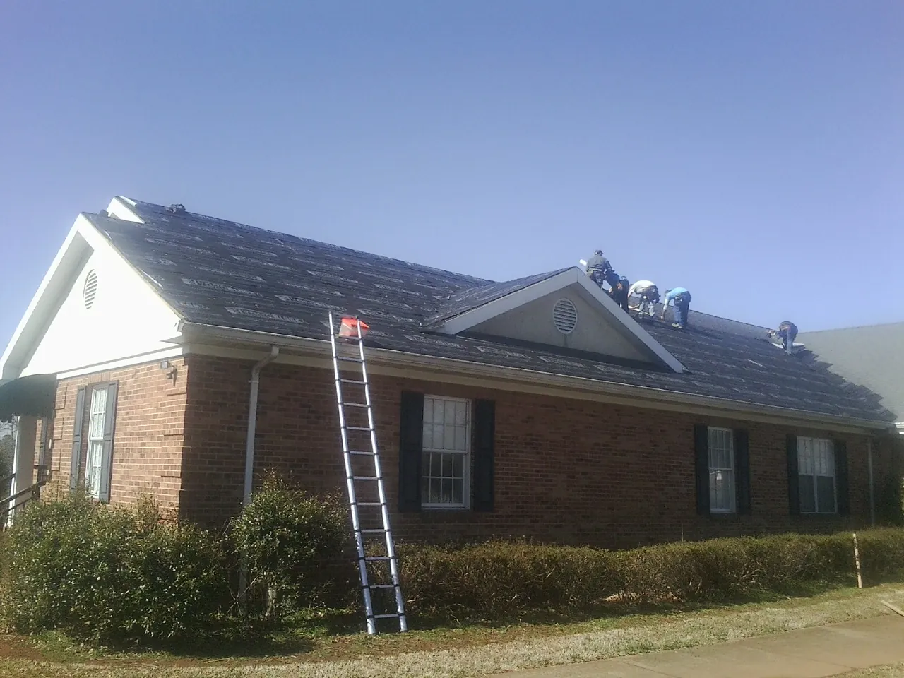 Crew tearing shingles off a brick ranch roof with a ladder set — Metal Roof Repair work by our crew in North Lewisburg