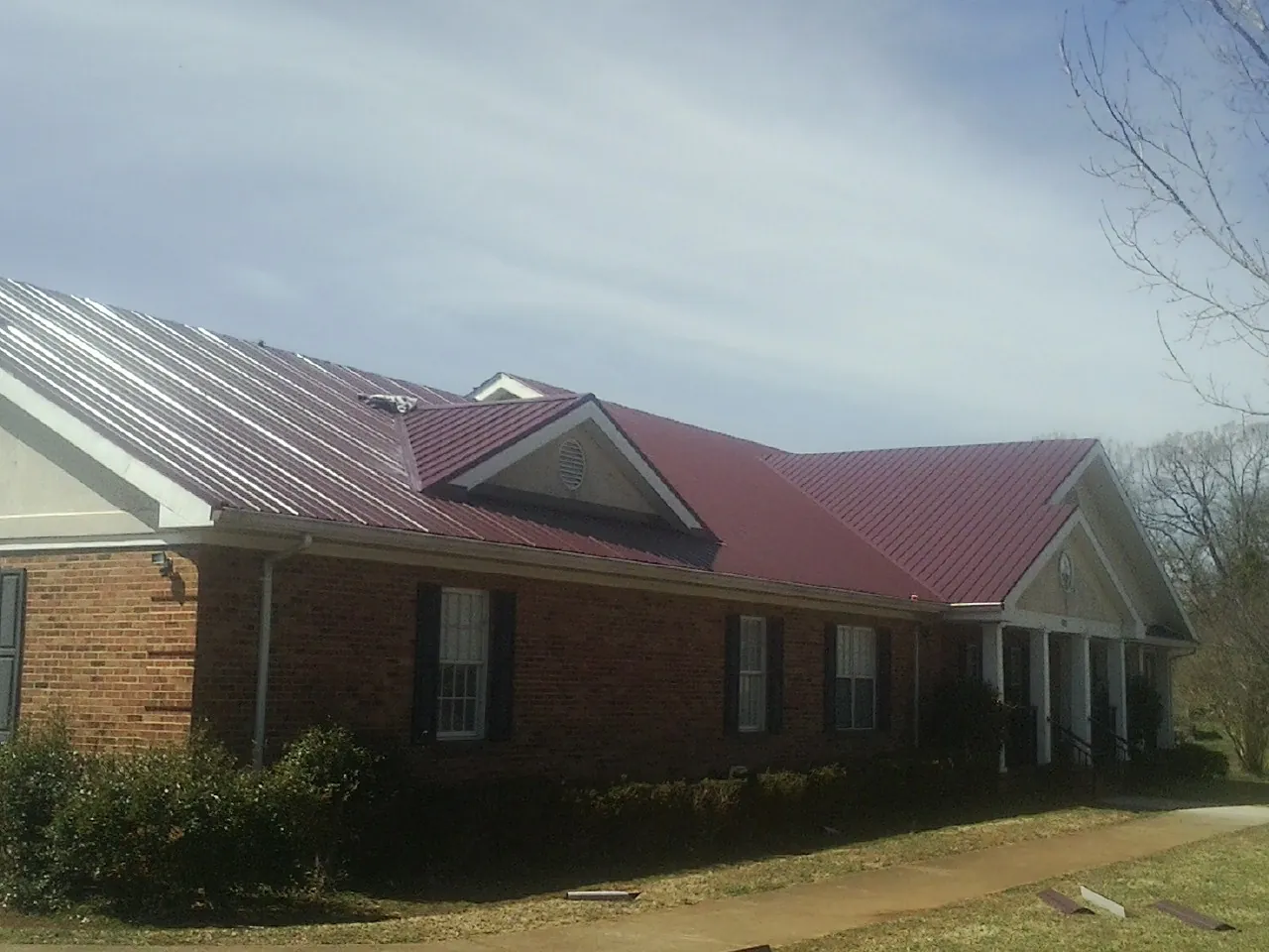 Red metal roof with gabled entries on a long brick building, from a Hail Damage Roof Repair job in North Lewisburg