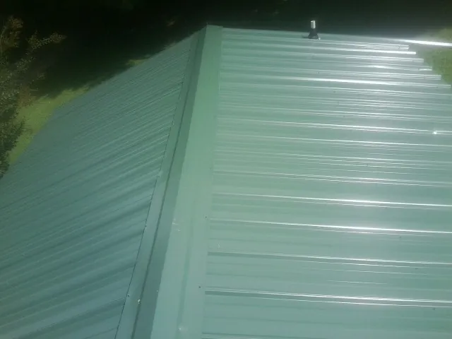 New green metal panels meeting at the ridge of a roof — Flat Roof Repair work by our crew in North Lewisburg
