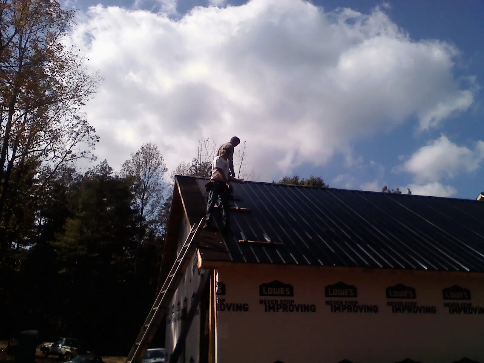 Roofer fastening dark metal panels high against a cloudy sky, from a Roof Inspection job in North Lewisburg