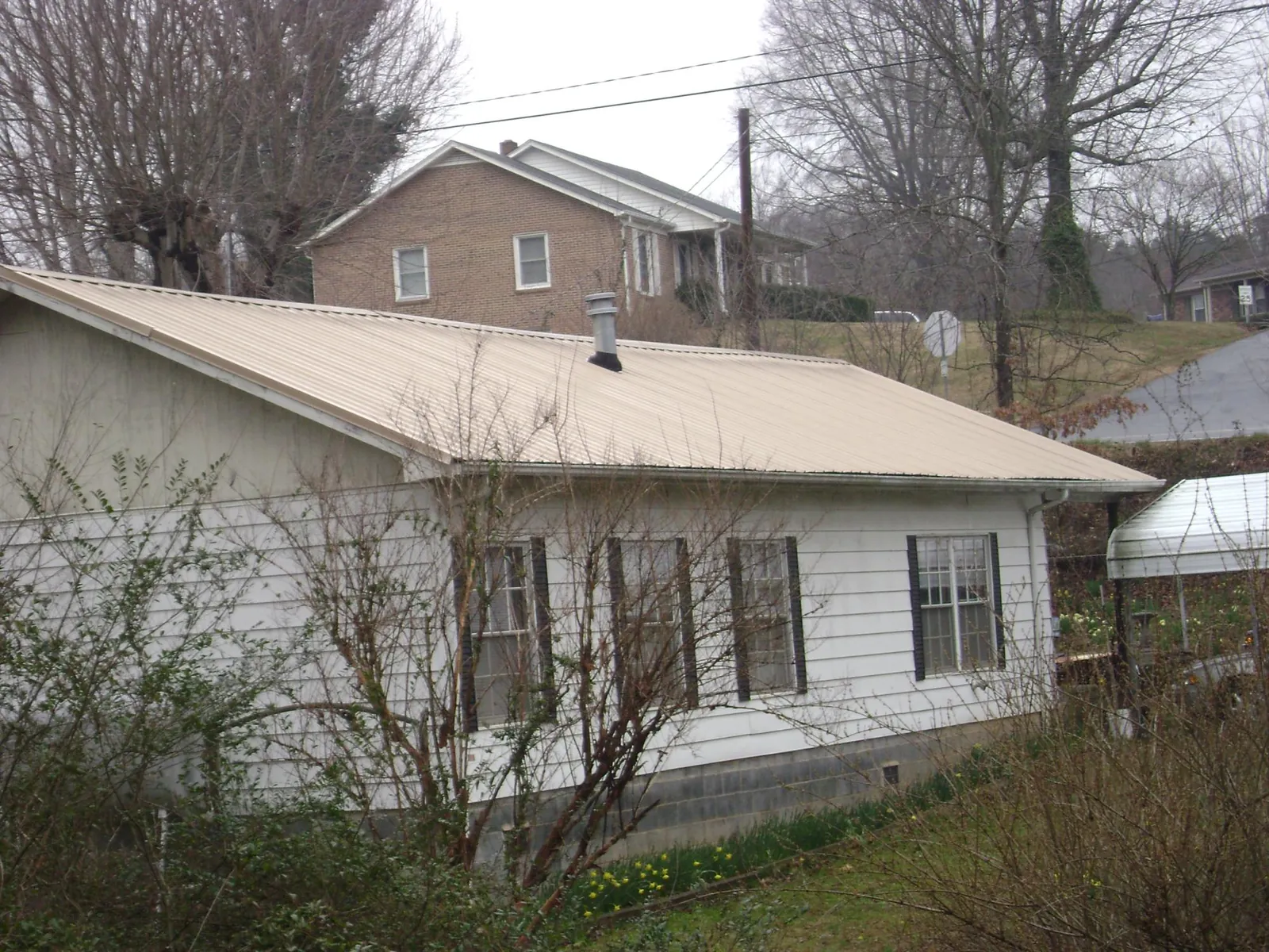 Tan metal roof on a white sided house set into a hillside — Commercial Roofing by Roofing Brothers in North Lewisburg